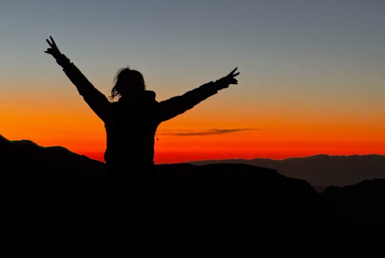Persona disfrutando del atardecer en la montaña con los brazos abiertos.