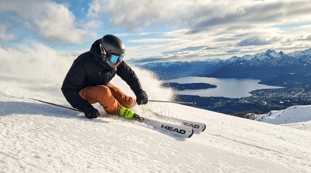 Bariloche en invierno. Esquiador girando en la nieve del Cerro Catedral en Bariloche, con el lago Nahuel Huapi de fondo