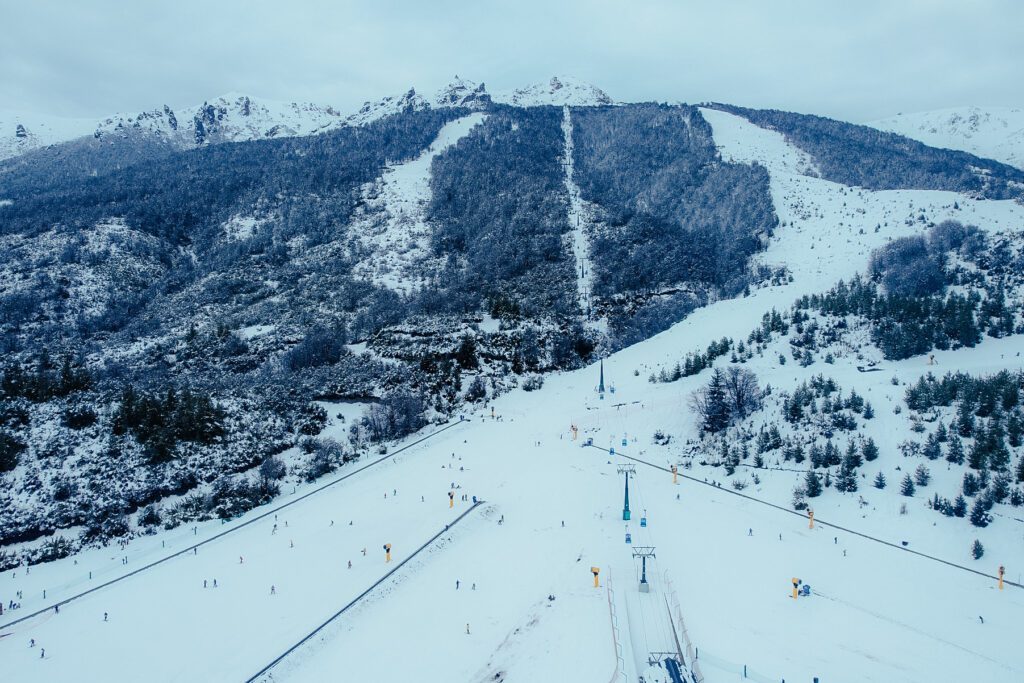 Pistas del Cerro Catedral entre bosque nevado y aerosilla, cordillera de fondo
