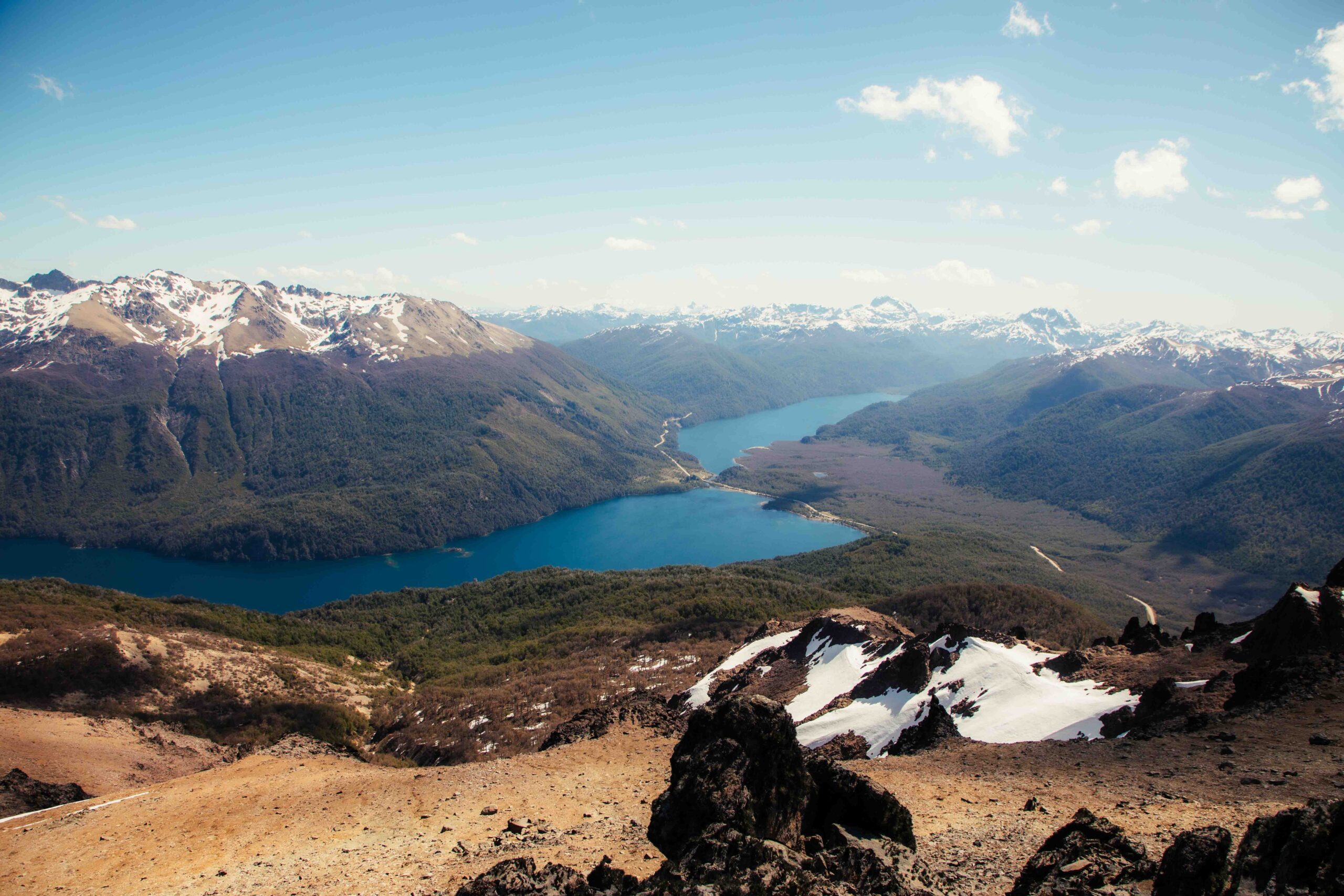 Vista desde el cerro Buque de dos lagos conectados entre montañas boscosas, con manchones de nieve en primer plano