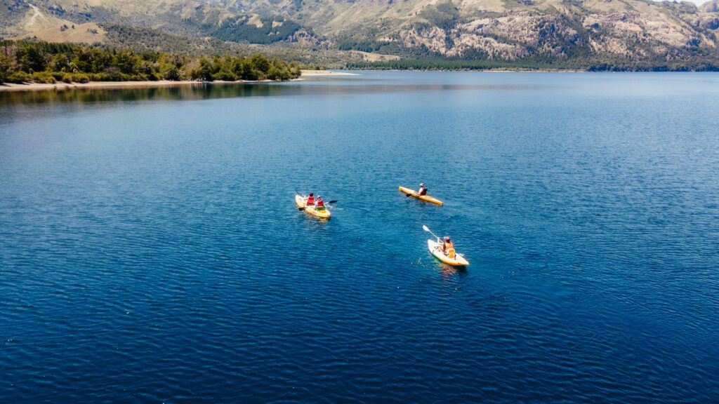Tres kayaks navegando las aguas azules de un lago patagónico, con la cordillera de fondo