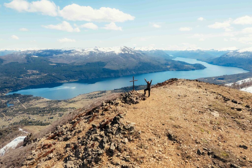 San Martín de los Andes. Cumbre del cerro Lolog con una cruz de madera y el lago Lolog abajo, rodeado de montañas con nieve