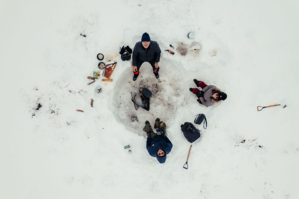 vista aérea de tres personas sentadas en la nieve en circrulo por comer un risotto