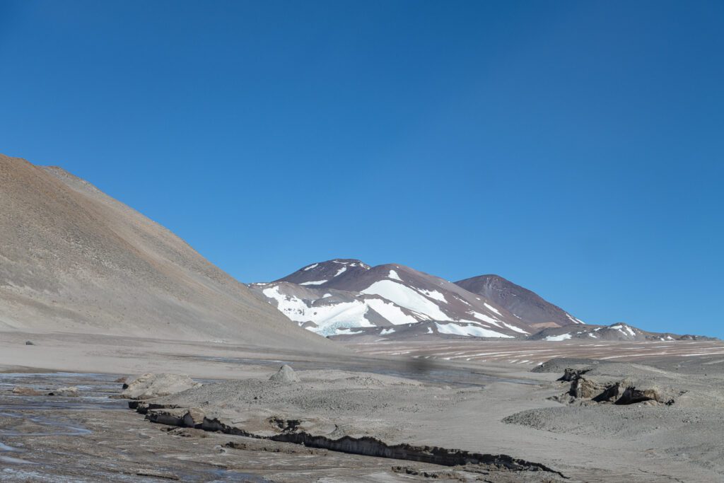 Picos nevados y glaciar de la cordillera riojana vistos desde una planicie de arena volcánica, cerca del Cráter Corona del Inca
