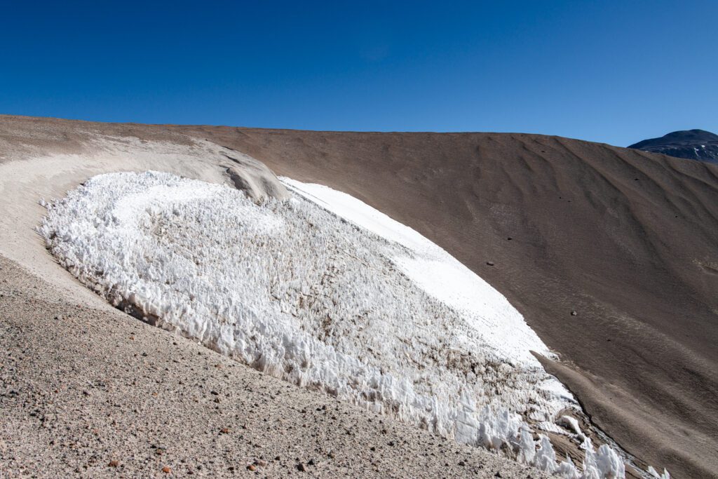 Borde de un ventisquero con formaciones de nieve dura recortadas contra una ladera de arena volcánica, en la alta montaña de La Rioja