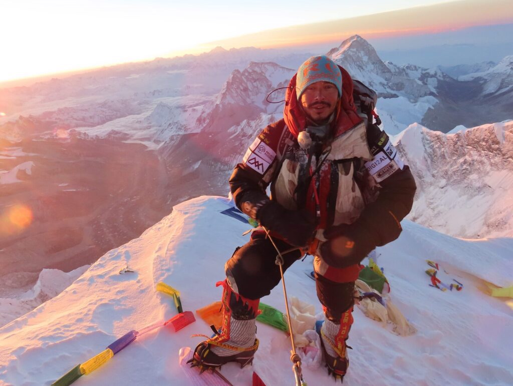 Nirmal Purja en la cumbre del Everest al amanecer, con el equipo de Project Possible y banderas de oración tibetanas junto a él