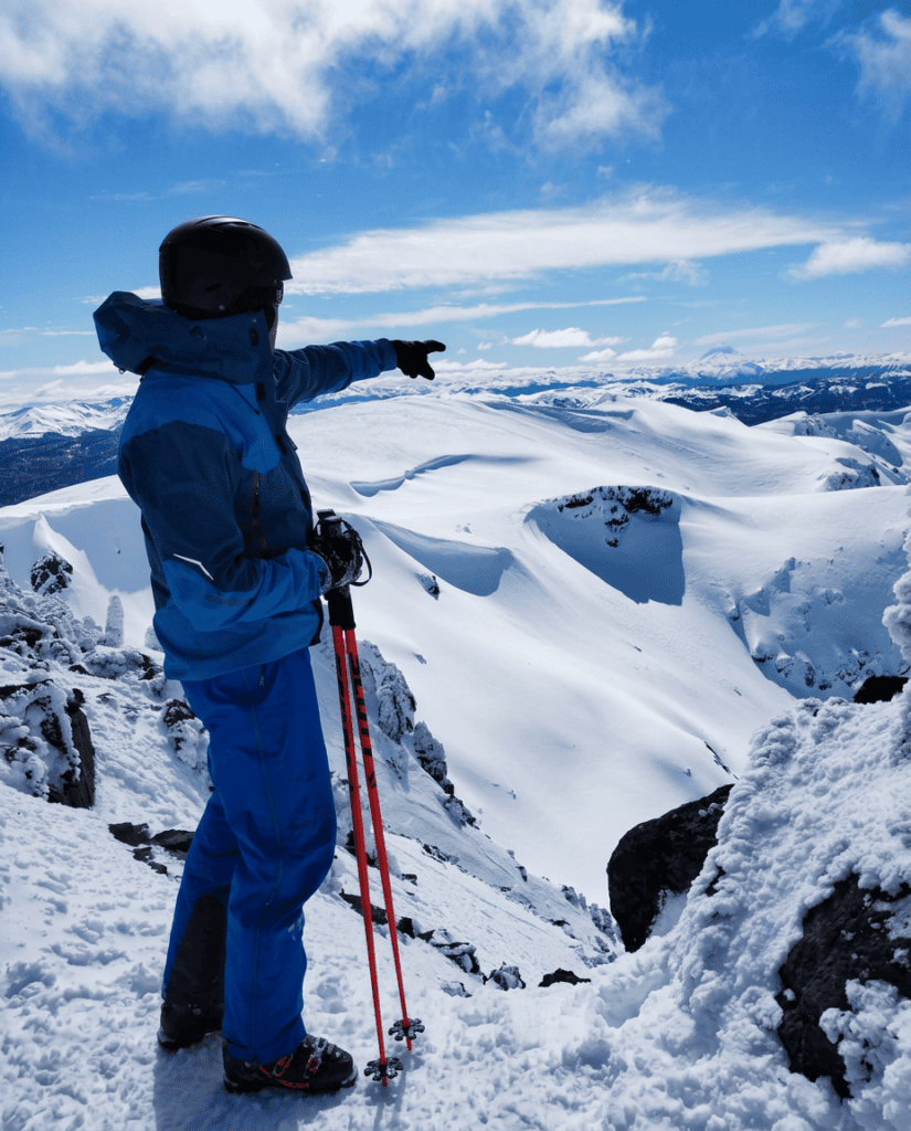Esquiador en la cumbre del cerro Ezpeleta señalando el horizonte, sobre un circo de nieve con la cordillera al fondo