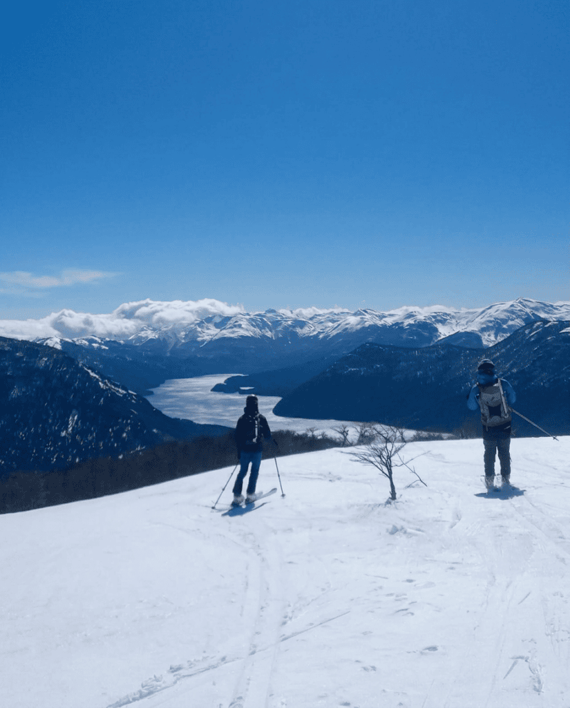 Dos esquiadores de travesía en la ladera del cerro Ezpeleta, con un lago y la cordillera nevada de fondo